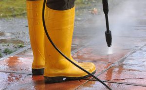 person wearing yellow rubber boots with high pressure water nozzle cleaning dirt tiles optimized 2000