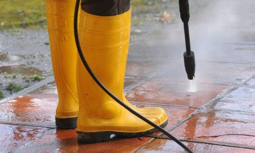person wearing yellow rubber boots with high pressure water nozzle cleaning dirt tiles optimized 2000